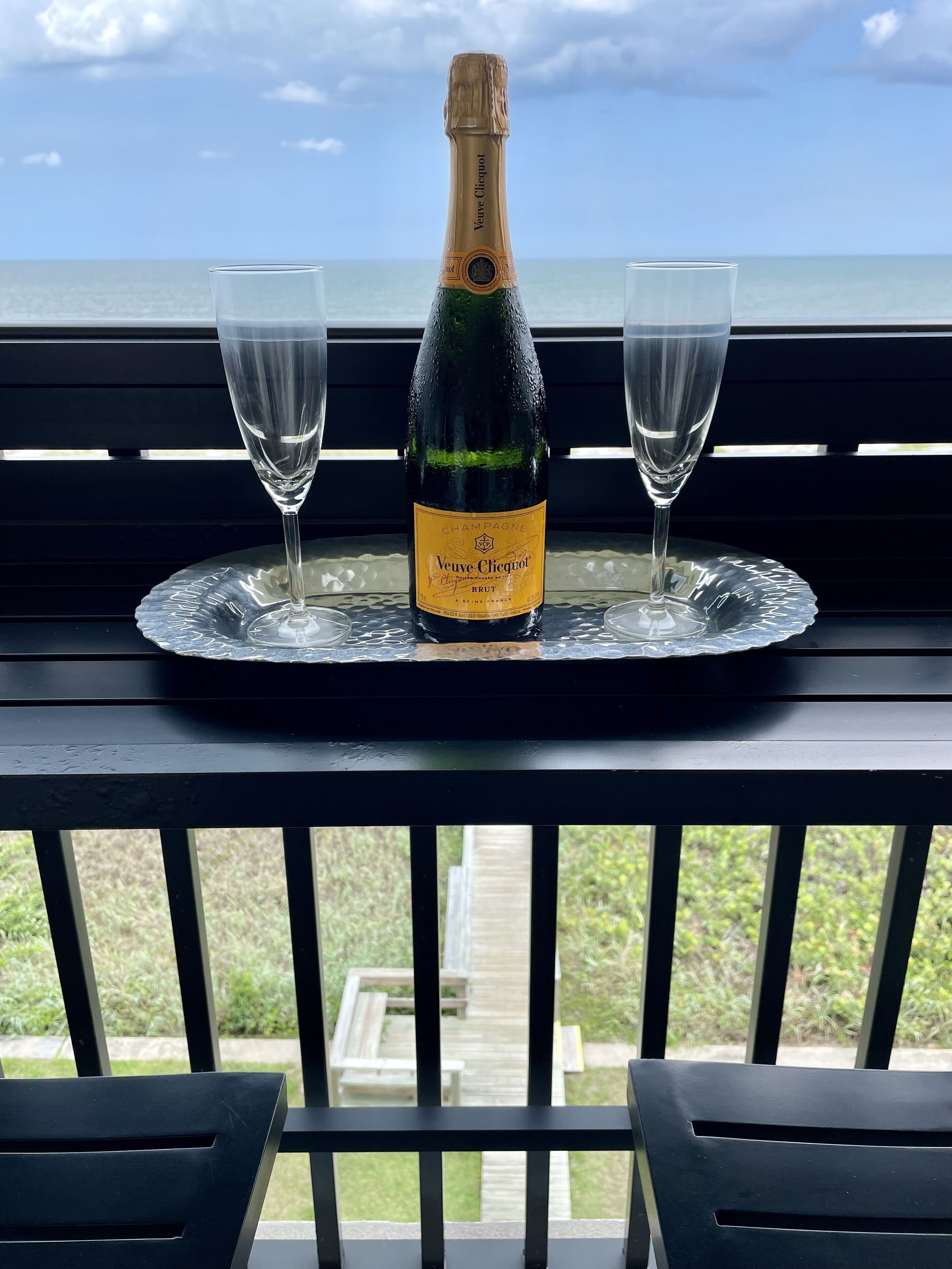 A bottle of Veuve Clicquot Brut champagne on a glass tray with two glasses on a balcony railing.