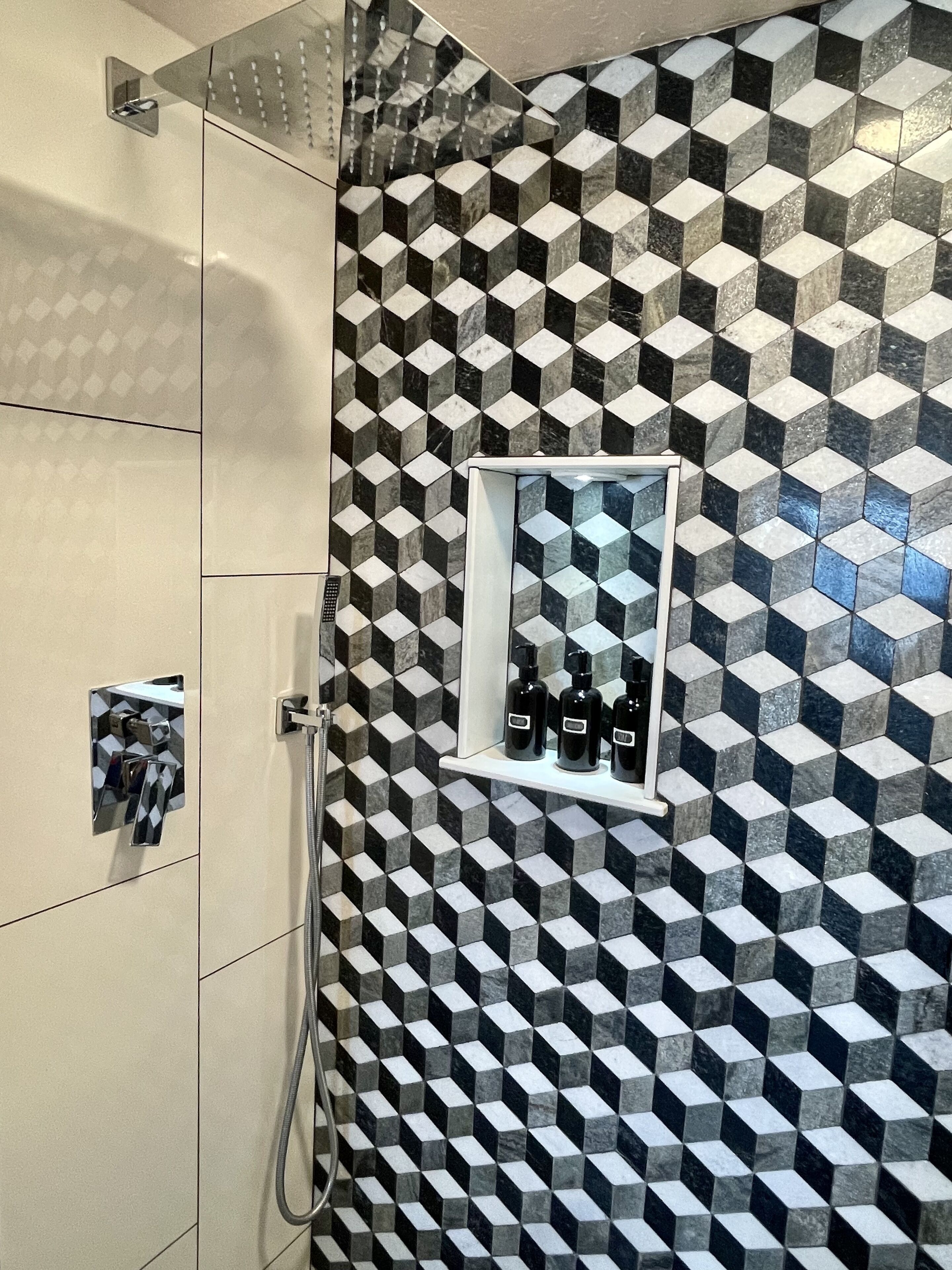 A bathroom with a geometric patterned wall, a shower area, and a shelf with toiletries.
