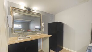 Una cocina compacta con un lavamanos, un espejo y un refrigerador.