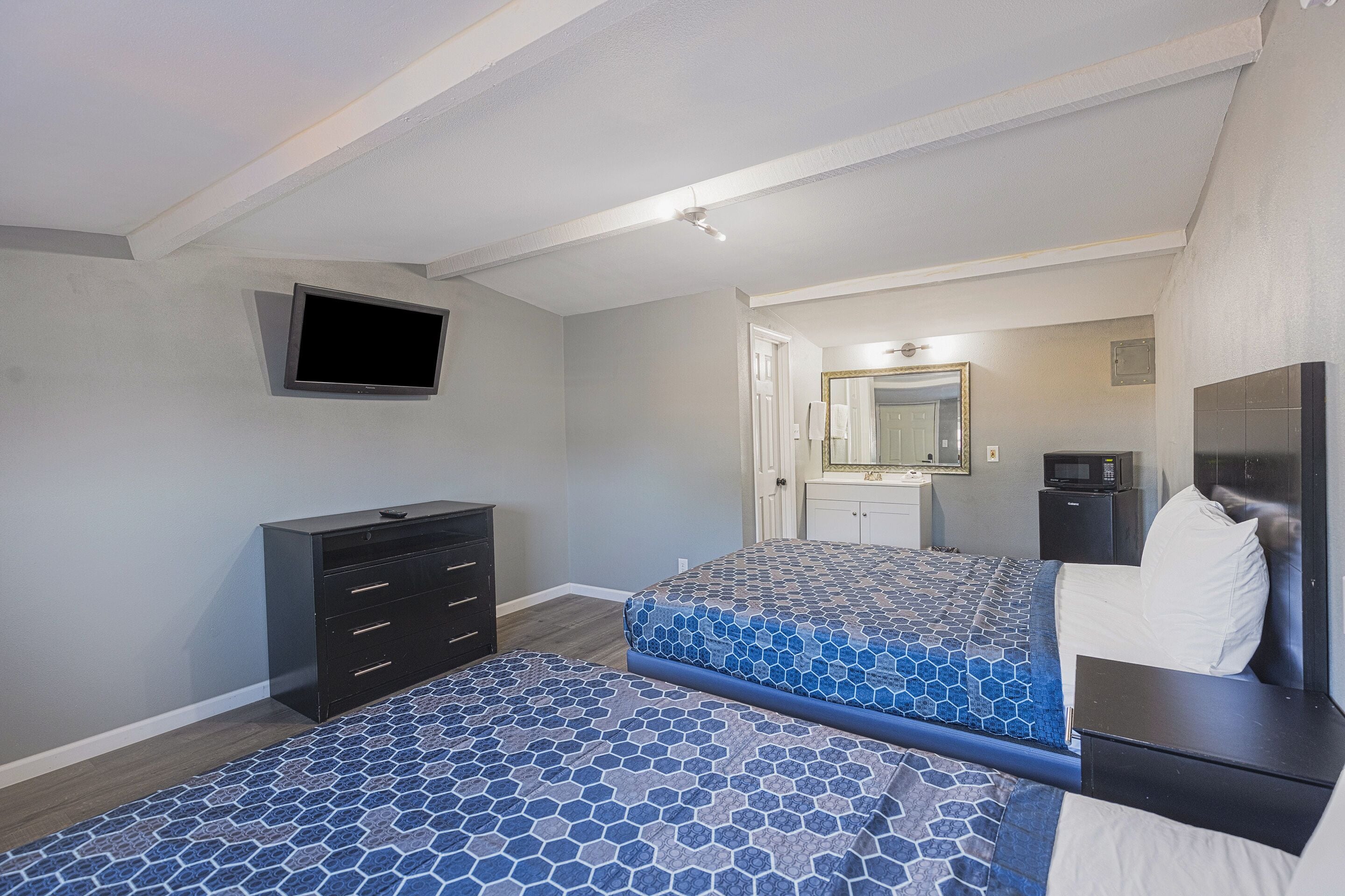 A bedroom with two beds, a dresser, a TV, a microwave, and a mirror.