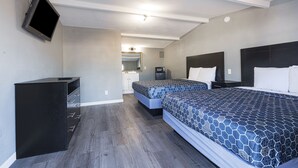Habitación de hotel con dos camas, un televisor montado en la pared, un escritorio y un espejo.