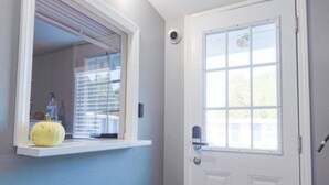 Un pasillo con una puerta blanca, una ventana con persianas y un estante con una calabaza.