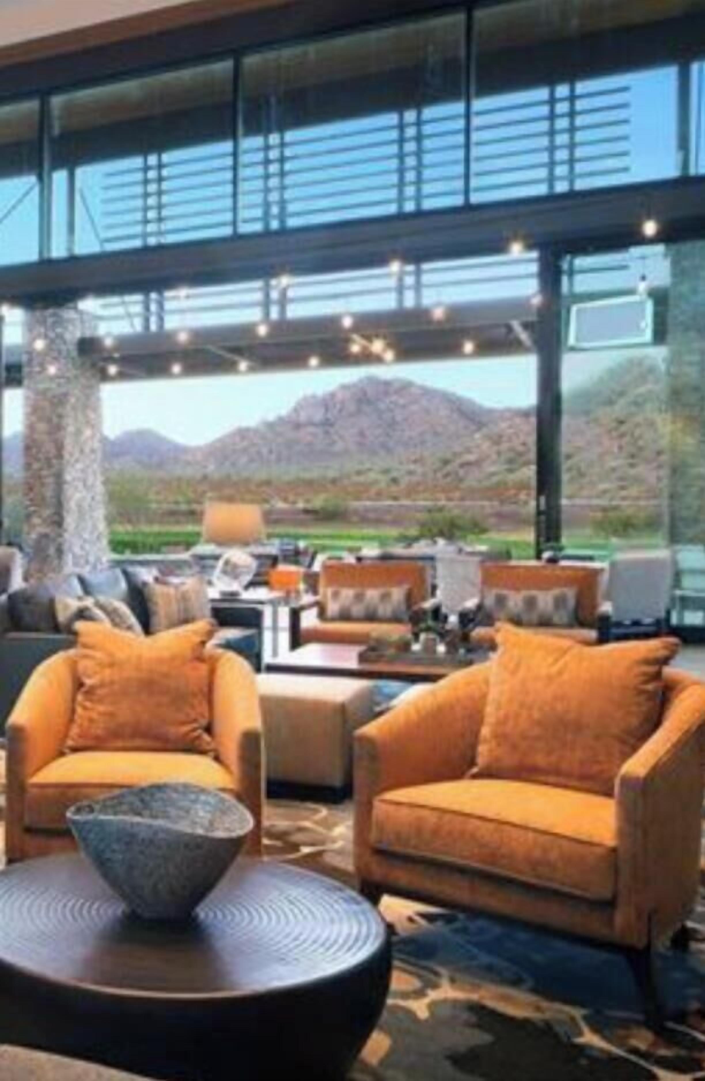 A modern interior with a large window, a stone bowl on a round table, and two orange armchairs.