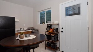 A compact kitchen with a dining table, a refrigerator, a stove, and a coffee maker. - Iron Horse Carraige Home & Parking (Tucson)