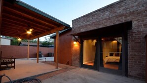 A covered patio area with a wooden bench, a hose, and a brick building with a glass door leading to a bedroom. - Iron Horse Carraige Home & Parking (Tucson)