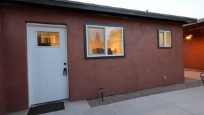 A single-story building with a brown exterior, a white door, and two windows with white frames. - Iron Horse Carraige Home & Parking (Tucson)