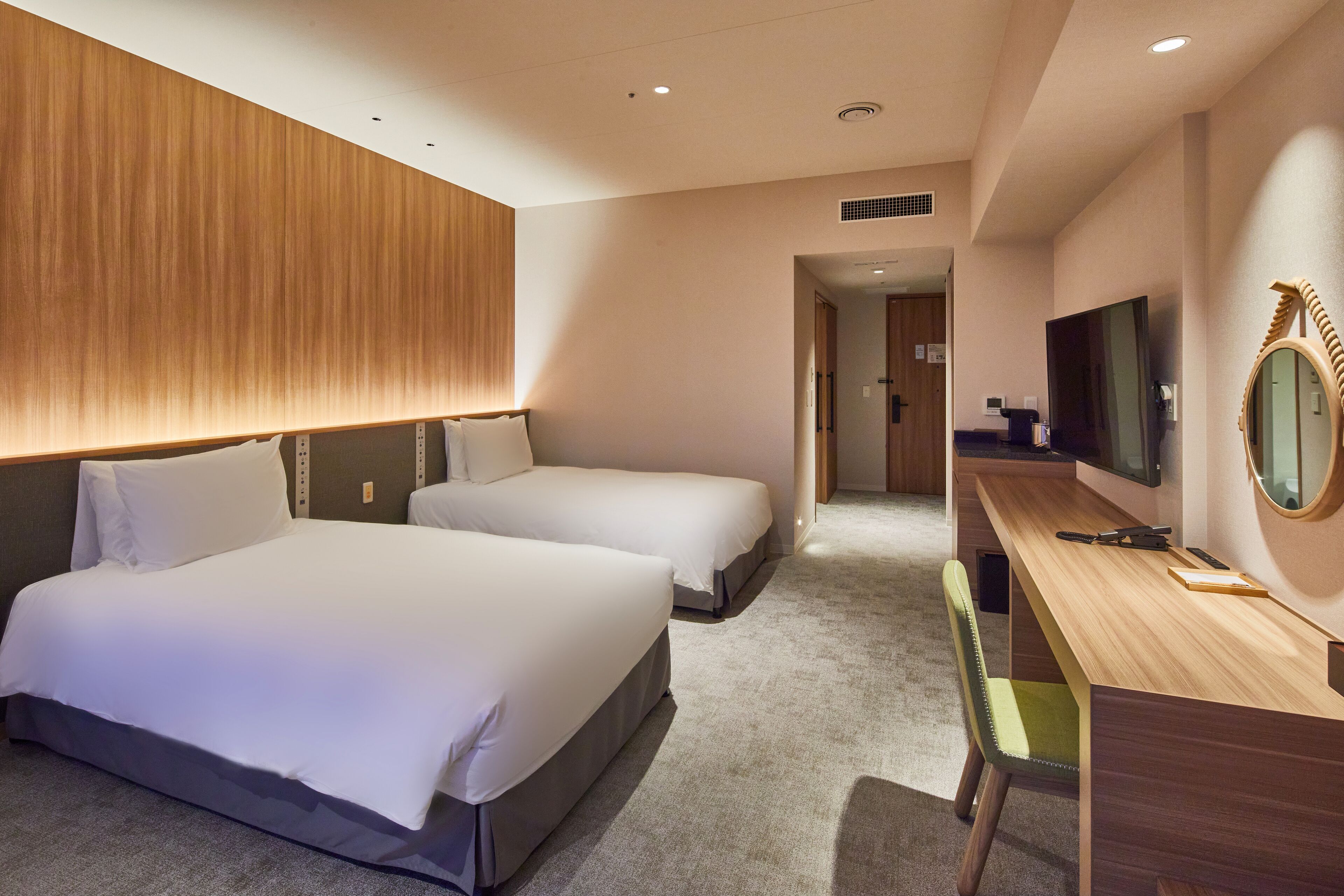 Habitación de hotel con dos camas, un escritorio, una silla, un televisor y un espejo.
