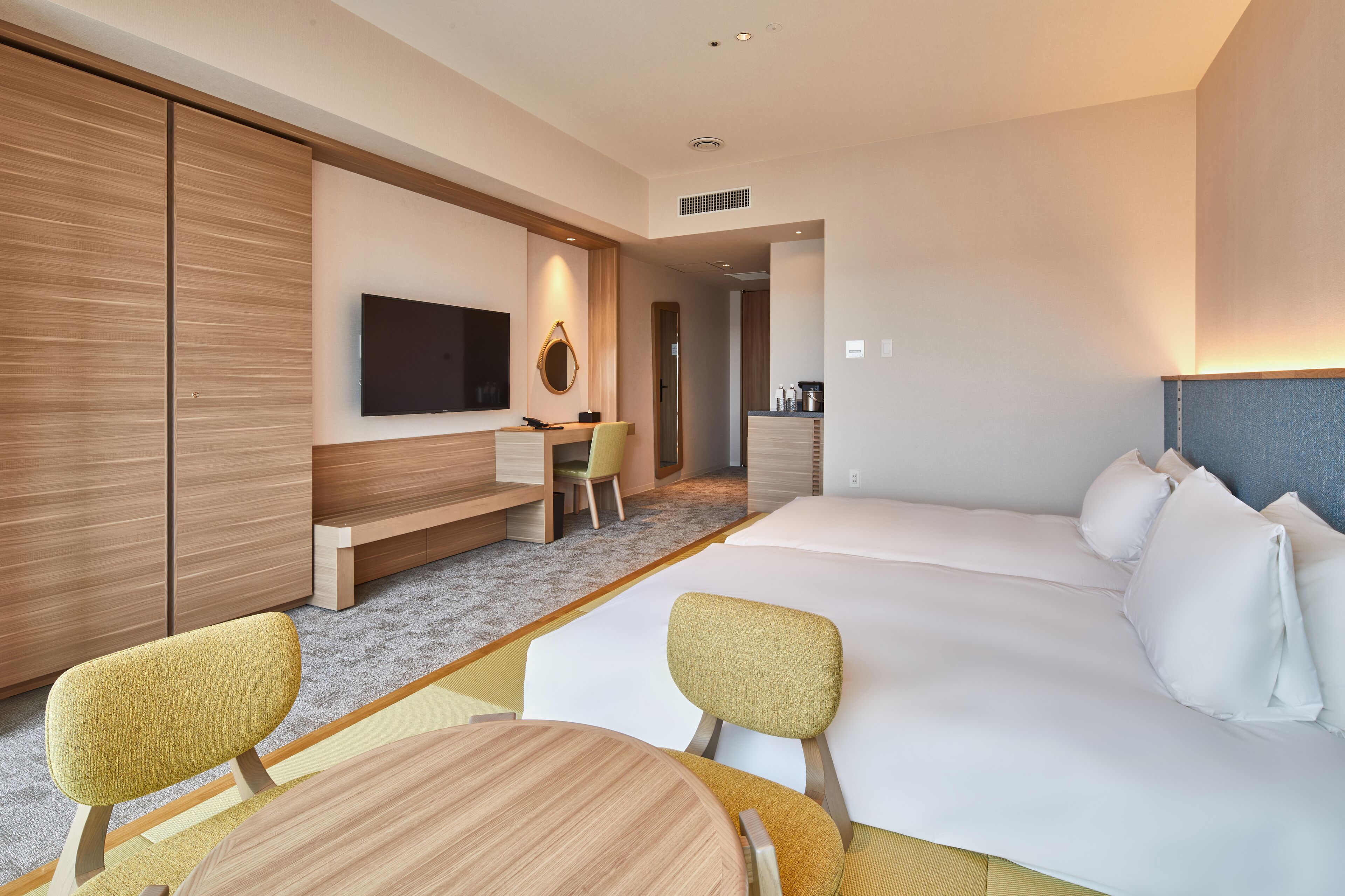 Una habitación de hotel moderna con una cama grande, un escritorio con silla, televisión y una kitchenette pequeña.
