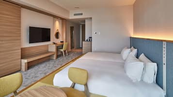 A hotel room with a large bed, a TV mounted on the wall, a desk with a chair, and a small seating area with a table and chairs.