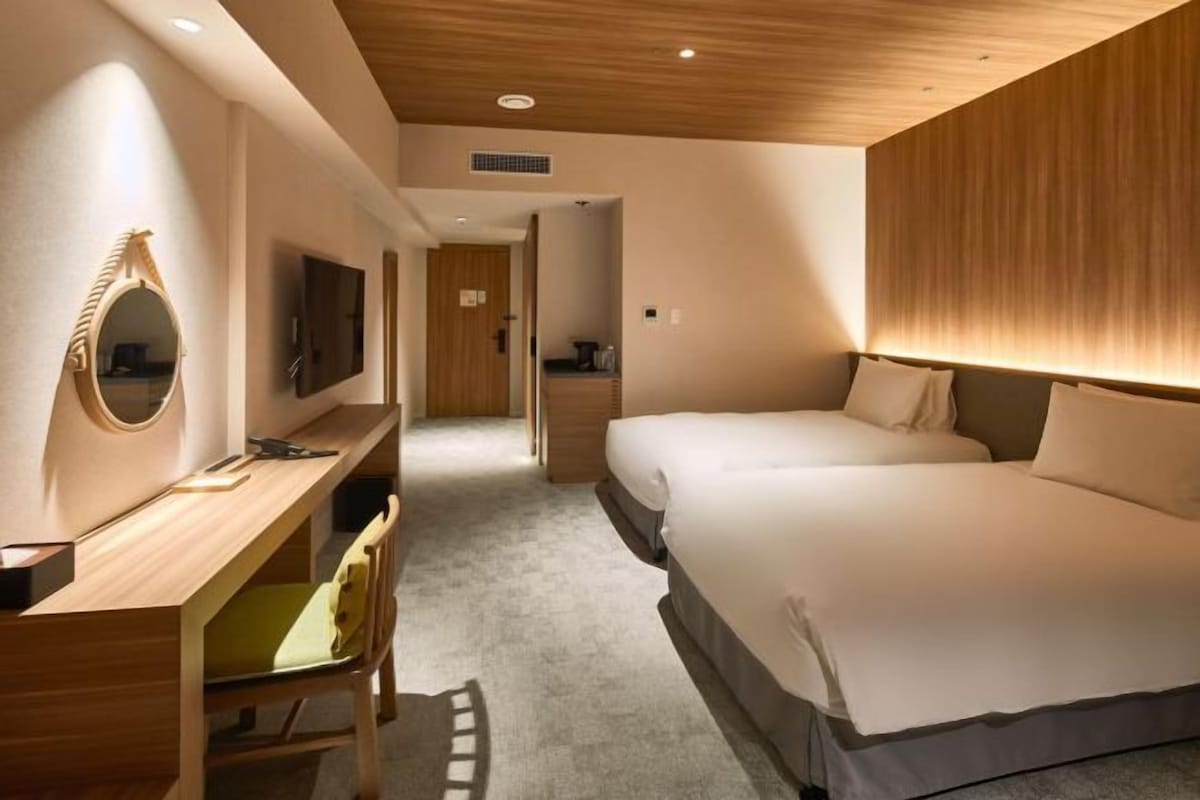 A hotel room with a wooden desk, a television, a bed, and a bathroom visible through an open door.