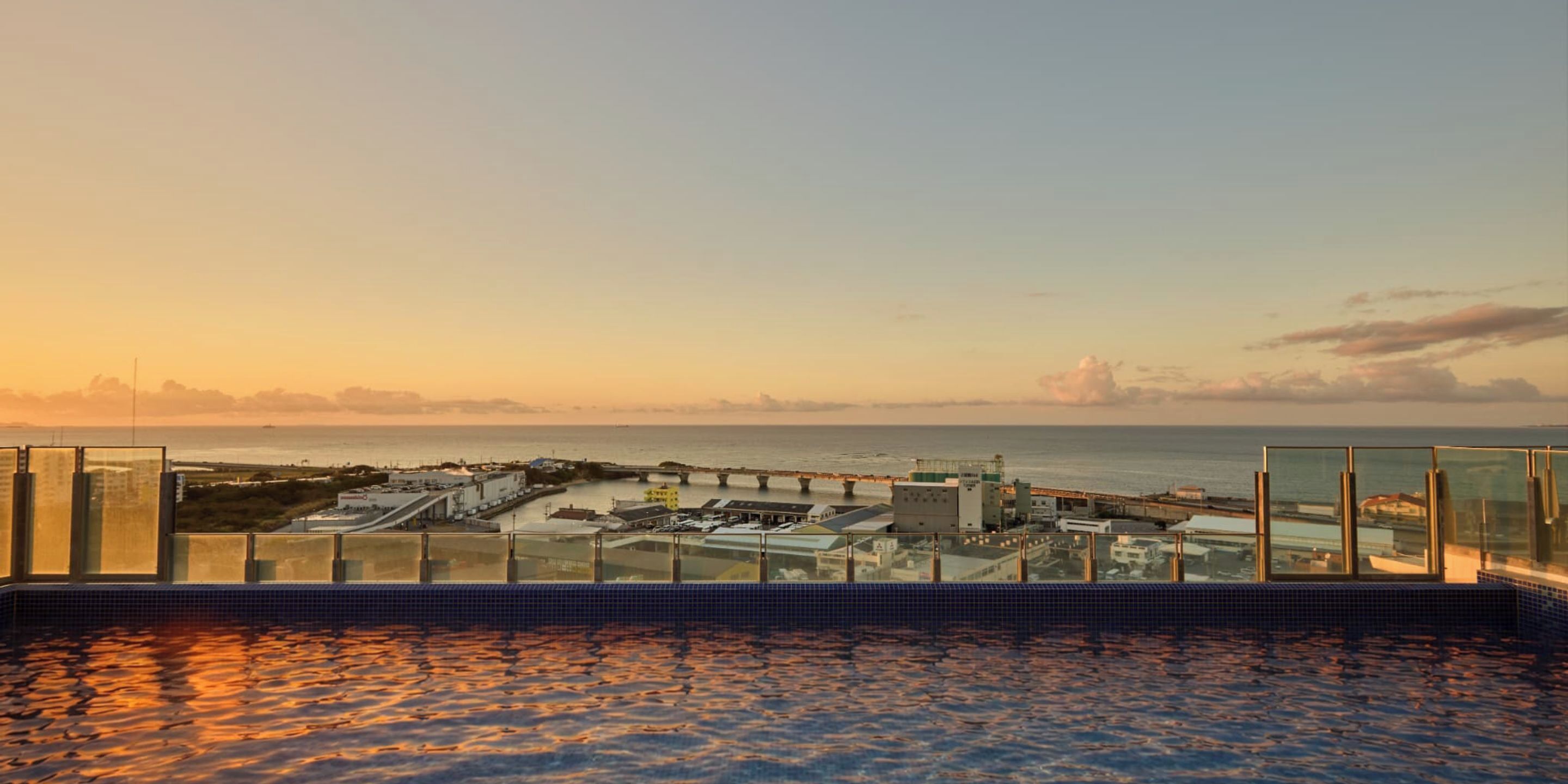 Piscina en la azotea con vista al océano y un puente al atardecer.