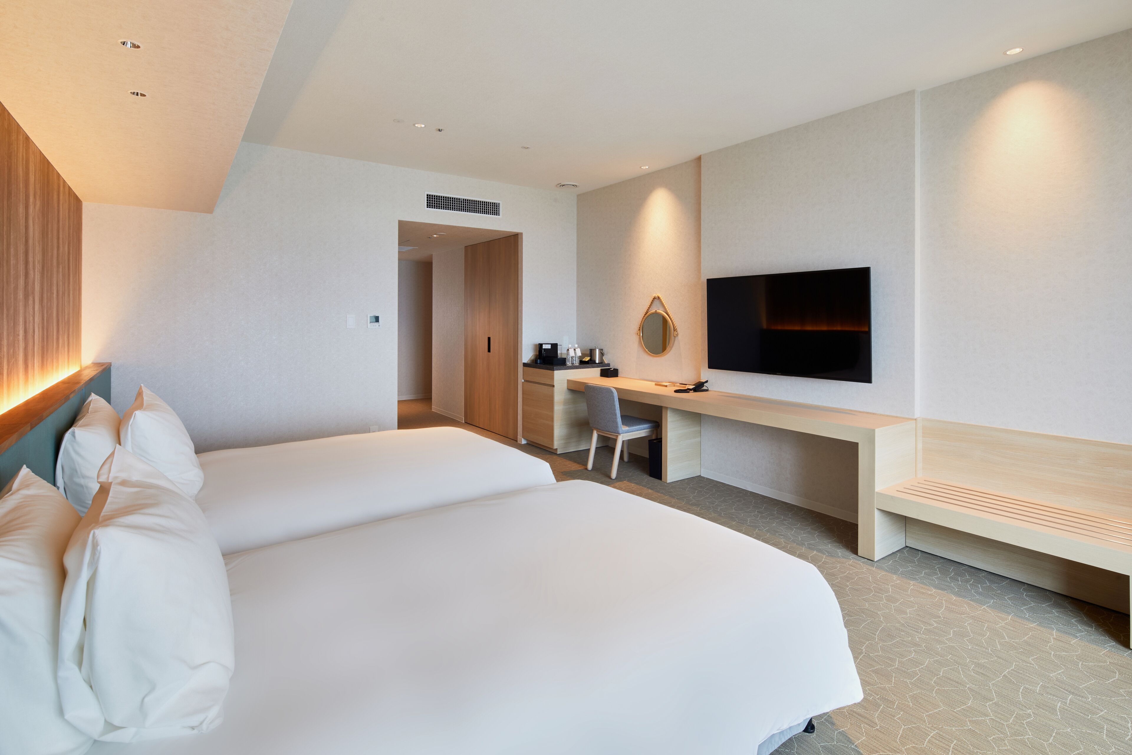 Habitación de hotel con dos camas, un escritorio, una silla, un televisor y una kitchenette pequeña.