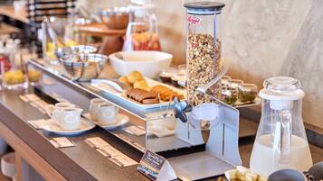 Een ontbijtbuffet met diverse soorten eten, zoals ontbijserialen, gebak en drankjes.