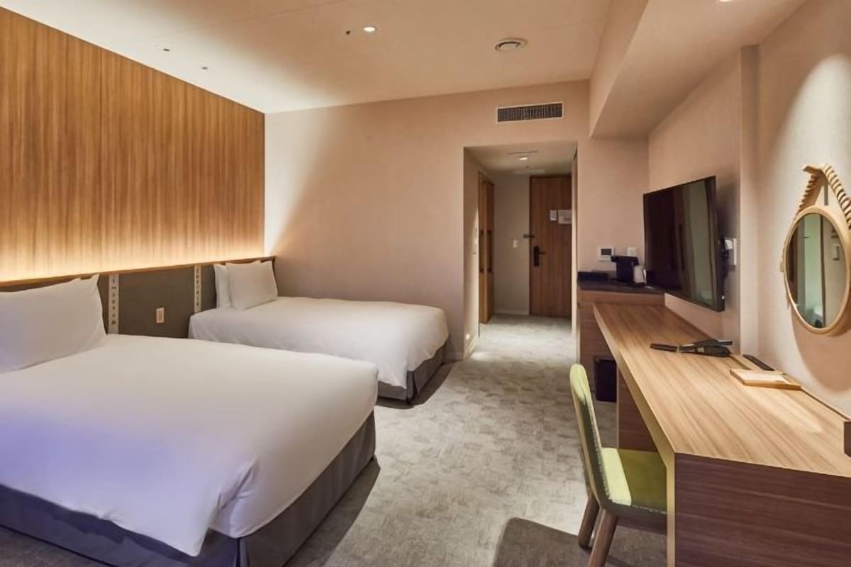 A hotel room with two beds, a desk with a chair, a television, and a mirror.
