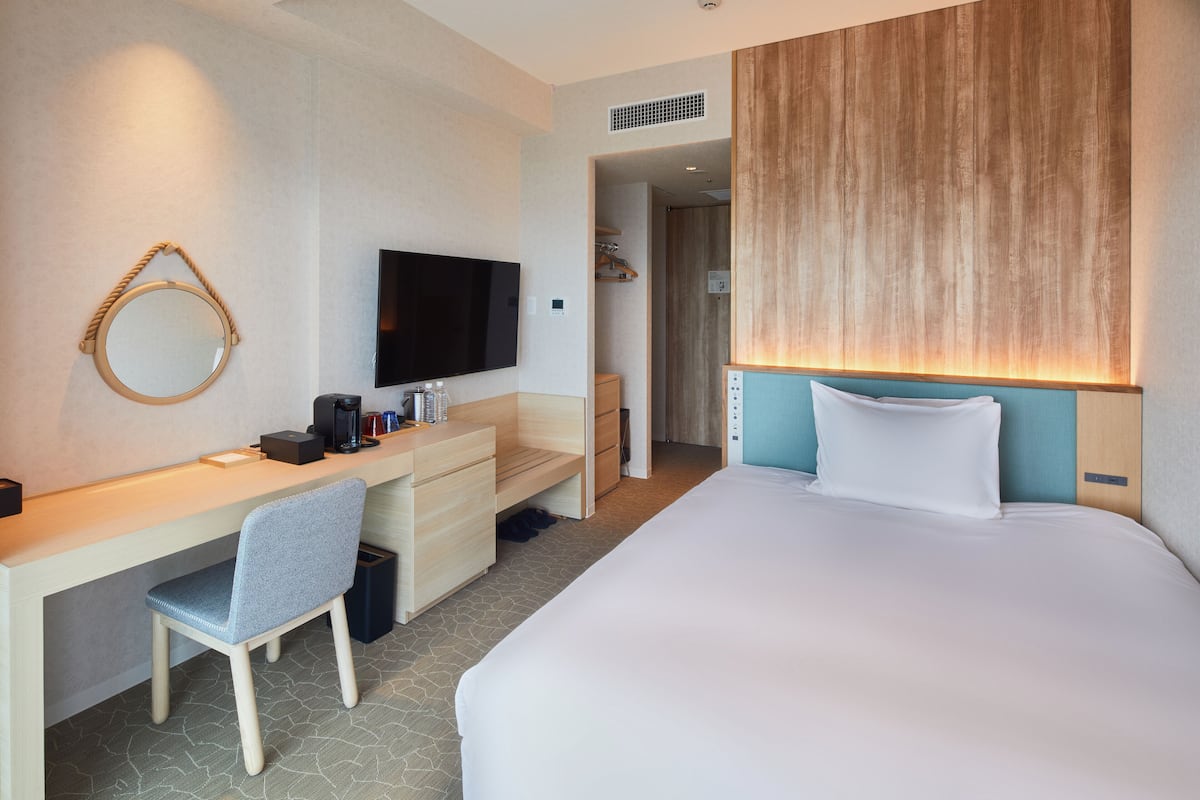 A hotel room with a bed, a desk with a chair, a television, and a mirror.