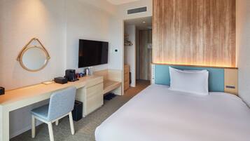 Quarto de hotel com cama, escrivaninha com cadeira, televisão e espelho.