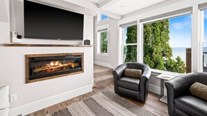 A modern living room with a fireplace, leather chairs, a TV, and large windows offering a view of the sea. - The Carriage House on Lake Superior  I  Lakeshore & Views  I  by Relax Open Air (Duluth)