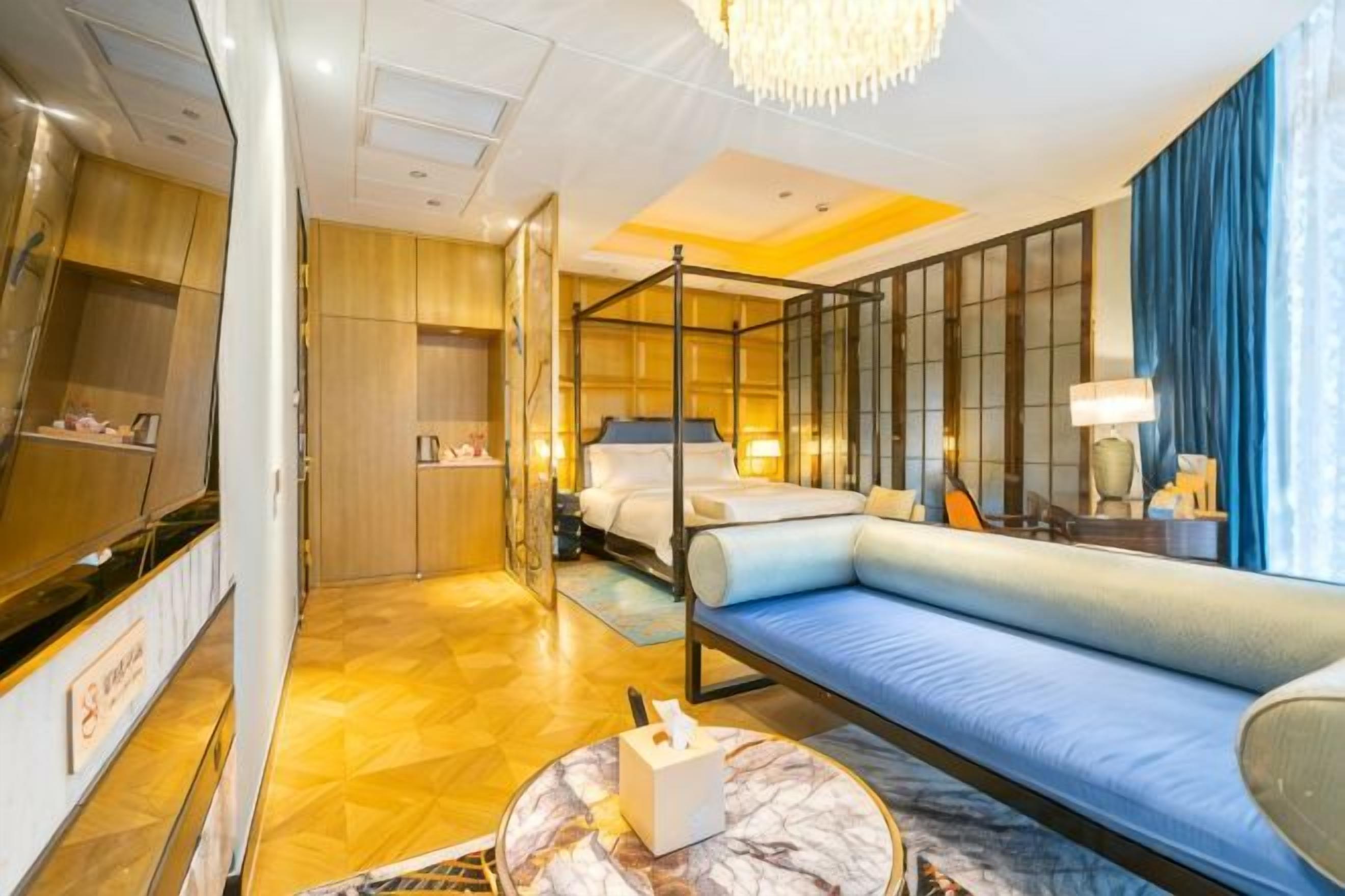 A hotel room with a four-poster bed, a sofa, a TV, and a minibar.