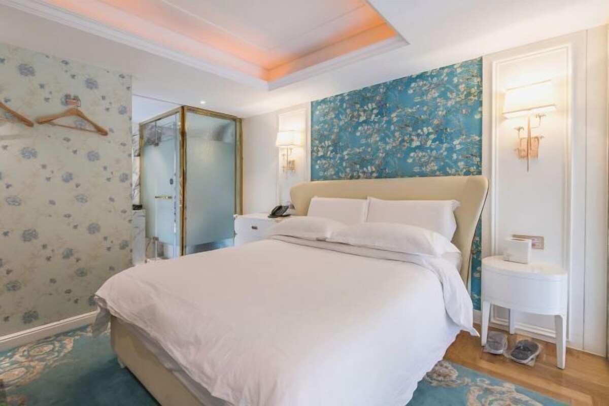A hotel room with a bed, bedside tables, a mirror, and a wall with a floral pattern.