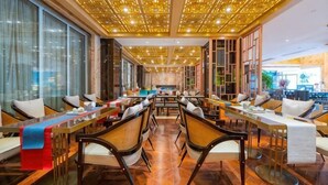 A restaurant with a long dining table, chairs, and a patterned ceiling.