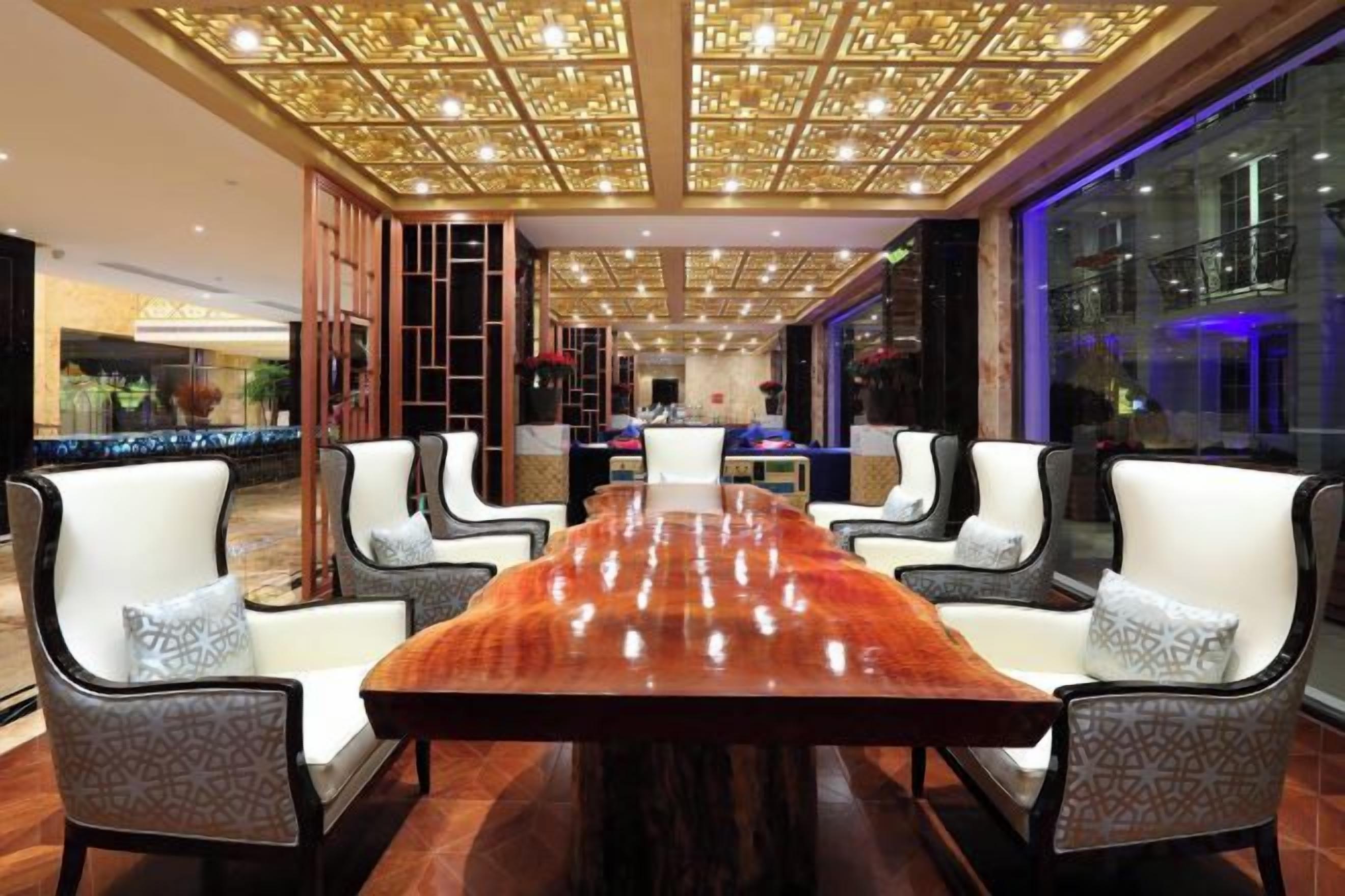 Un comedor amplio con una larga mesa de madera rodeada de sillas, un techo decorativo y ventanas grandes.