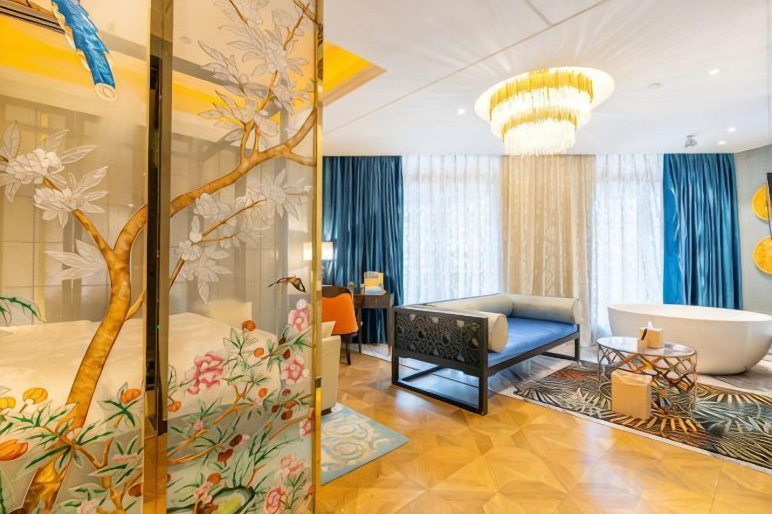 A modern hotel room with a large bed, a sitting area, a bathtub, and a decorative screen with floral patterns.