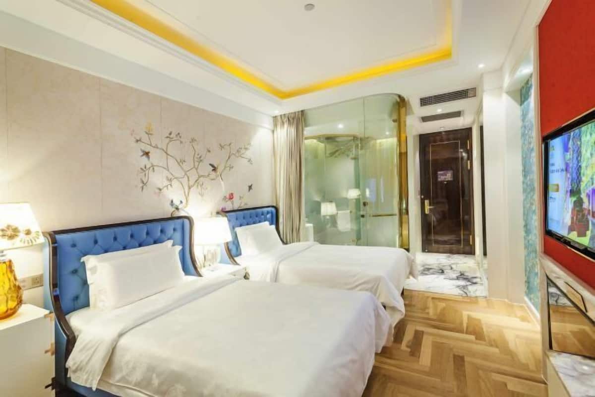 A hotel room with two beds, a TV, a glass shower enclosure, and a marble floor.