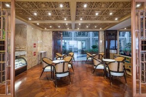 An indoor dining area with wooden flooring, multiple tables and chairs, and a view through a glass door to an outdoor space. - International Milan (Deqing)