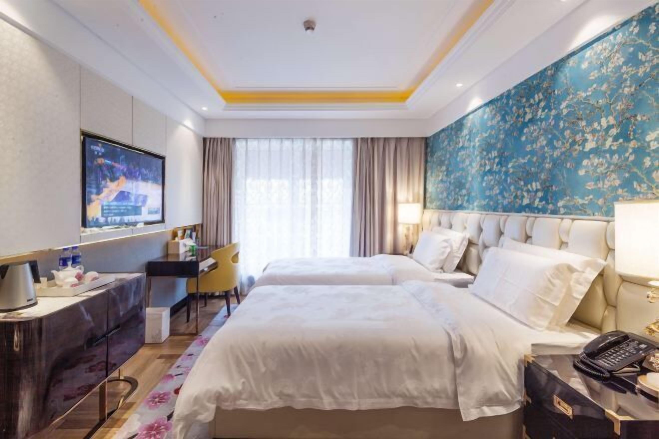 A hotel room with a bed, a desk, a chair, a TV, and a window with curtains.