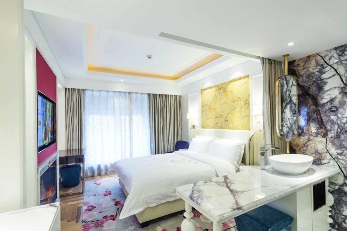 A modern hotel room with a large bed, a bathroom with a marble vanity, and a large window with curtains.