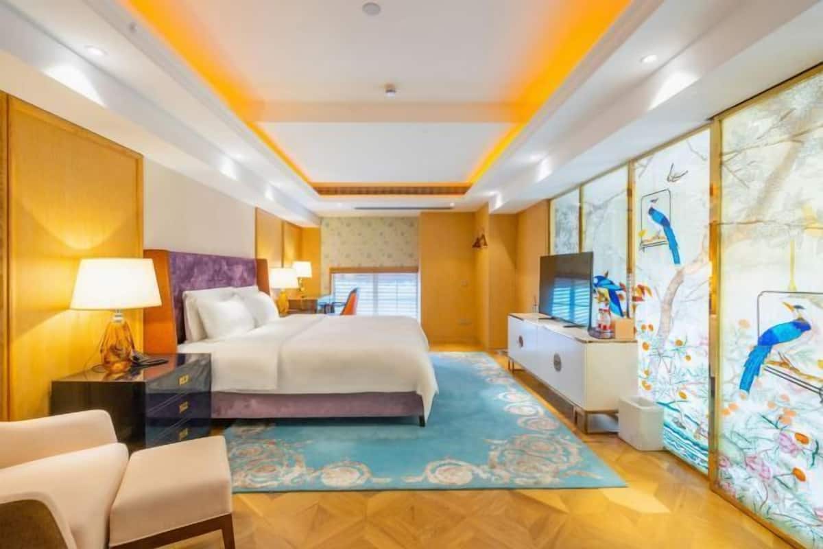 A hotel room with a bed, bedside tables, a desk, a TV, and a large window.