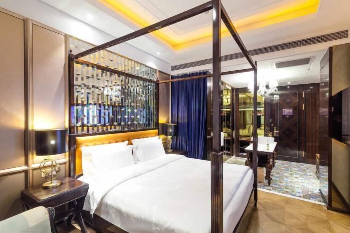 A four-poster bed with a headboard, a bedside table, a mirror, and a small desk with a chair.