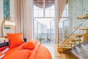A bedroom with a bed, a window with a view of buildings, a staircase, and a balcony with a railing. - International Milan (Deqing)