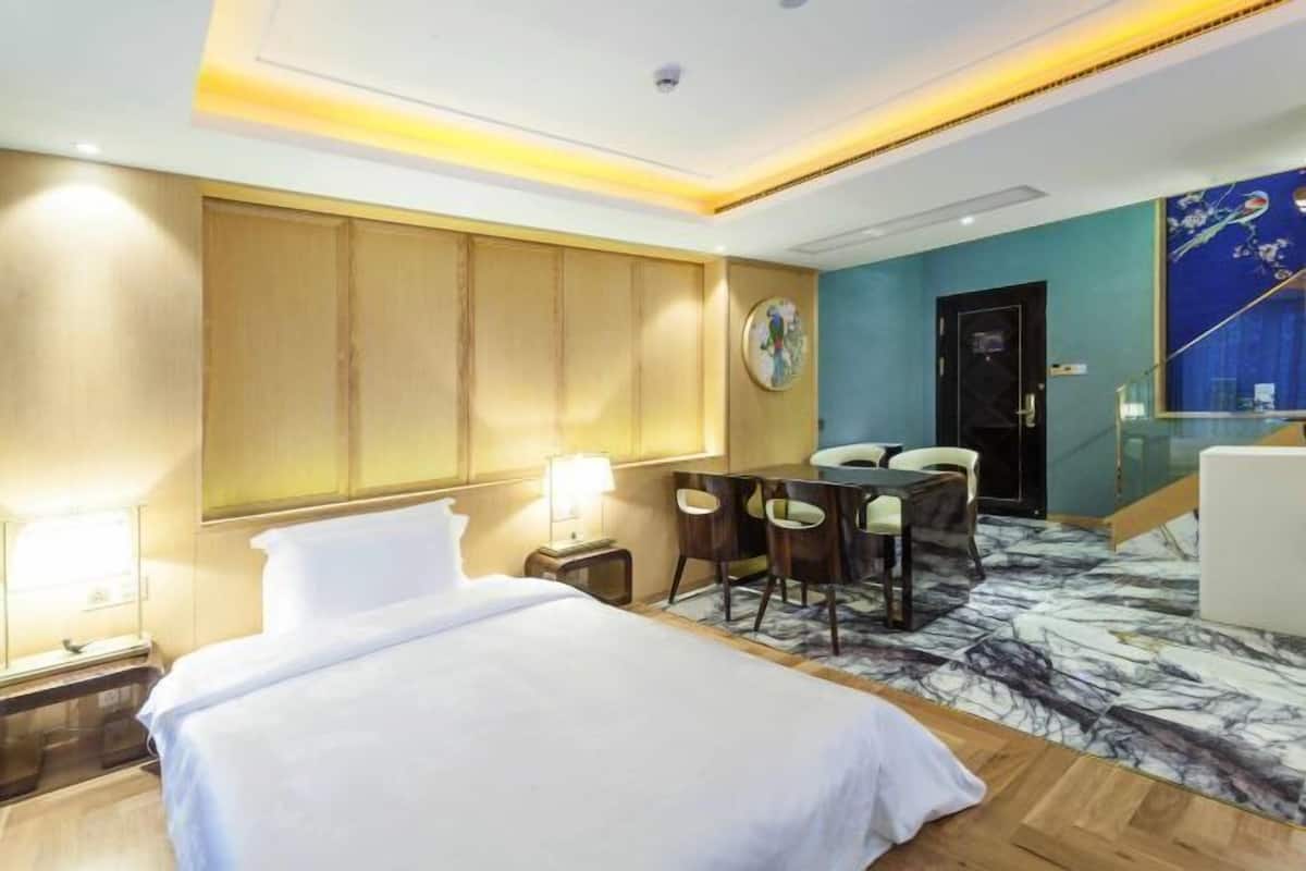 A hotel room with a bed, desk, chairs, and a clock on the wall.