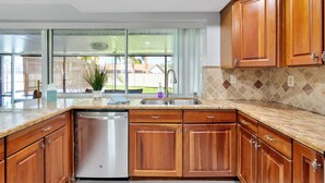 Una cocina con armarios de madera, lavavajillas de acero inoxidable, un lavabo y una ventana con vistas al exterior.