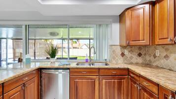 A kitchen with wooden cabinets, a stainless steel dishwasher, a sink, and a window with a view of the outside.