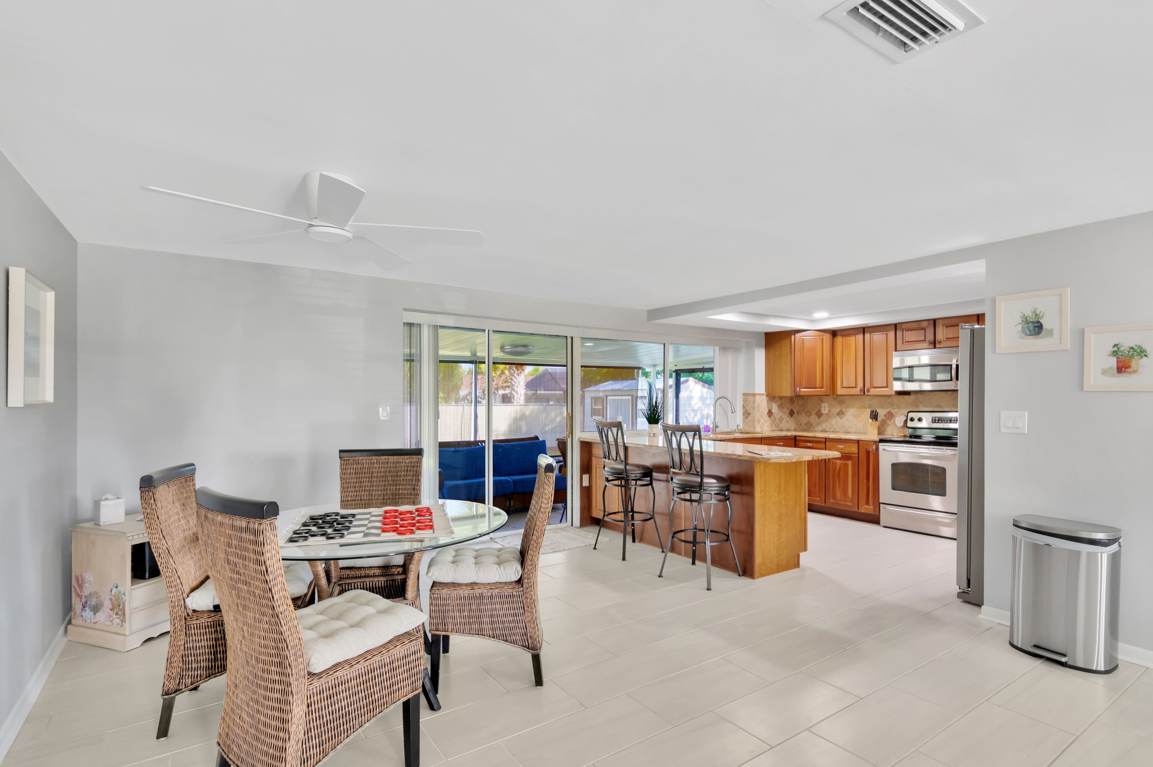 A modern kitchen with stainless steel appliances, a dining area with wicker chairs, and a glass-top table.