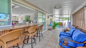Un patio techado con barra, sillas de mimbre, un sofá azul y una mesa de comedor con sillas.