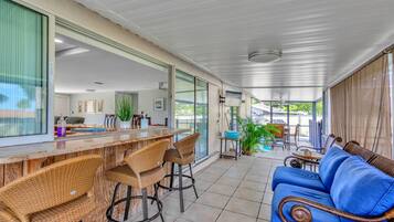 A covered patio area with a bar, wicker chairs, a blue sofa, and a dining table with chairs.
