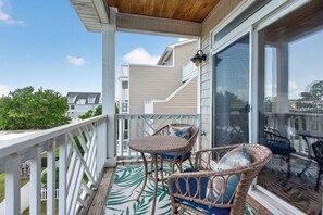 A covered balcony with wicker furniture, a glass door, and a view of neighboring houses.