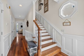 A hallway with a wooden staircase, white walls, and a bench.