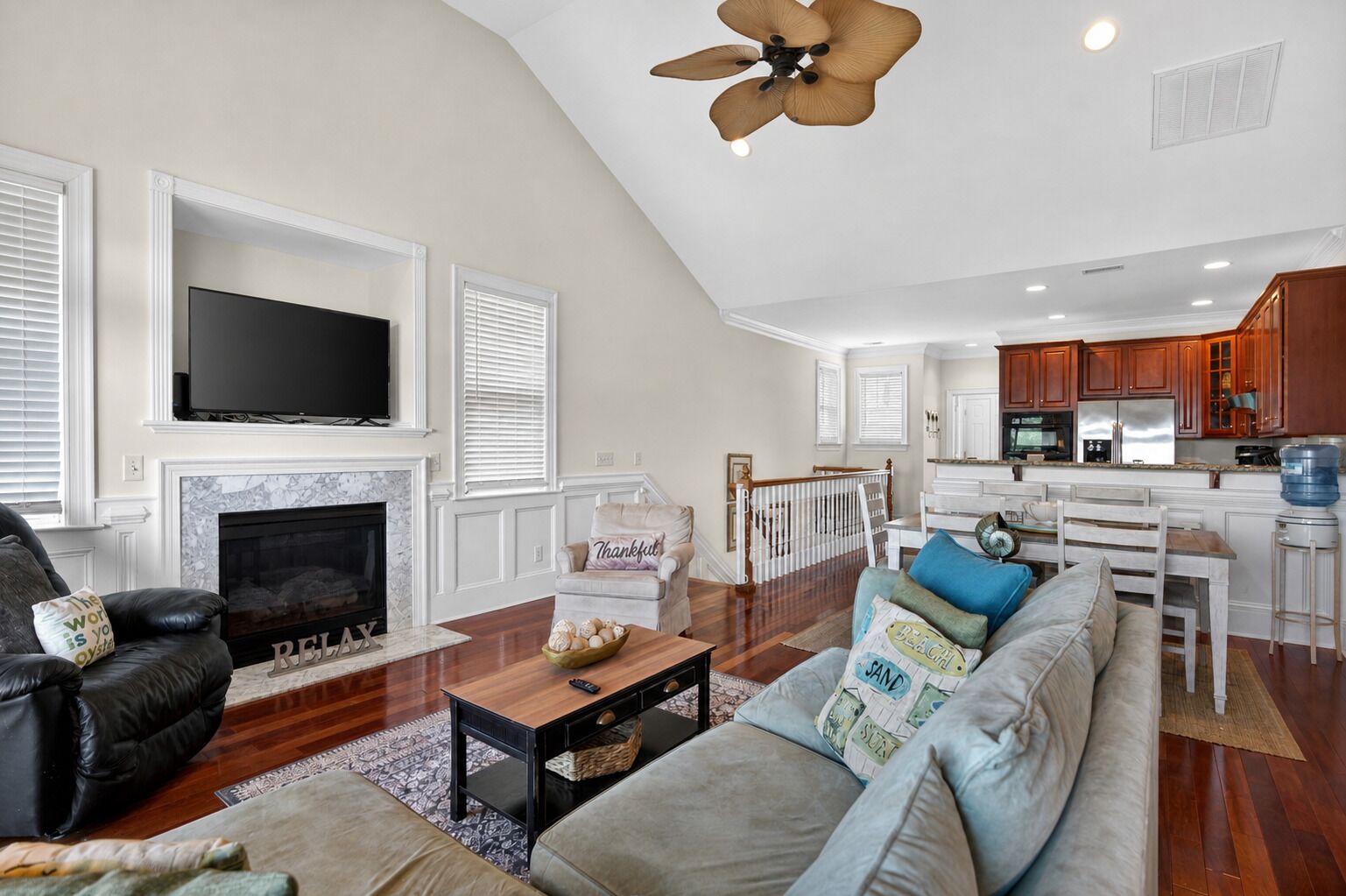 A spacious living room with a fireplace, a television, and a kitchen area with wooden cabinets.