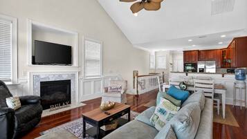 A spacious living room with a fireplace, a television, and a kitchen area with wooden cabinets.