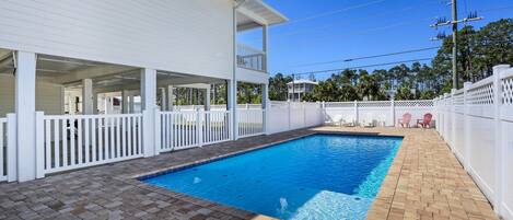 A swimming pool with a white fence, a covered patio area, and a brick patio.