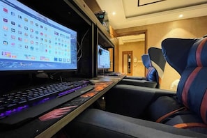Ein Hotelzimmer mit Schreibtisch, zwei Monitoren, Tastatur und Stuhl.