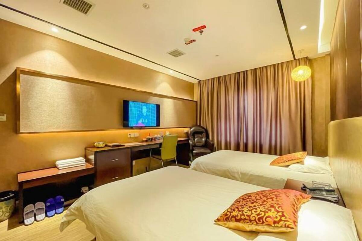 A hotel room with two beds, a desk, a chair, a television, and a wardrobe.