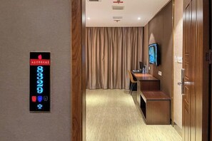Un pasillo de hotel con un panel de número de habitación digital, un televisor montado en la pared y un mostrador de recepción.