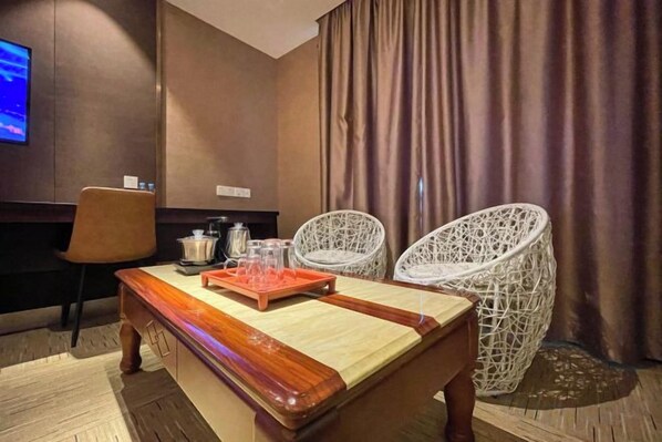 A hotel room with a wooden table, two wicker chairs, a TV, and a curtain.