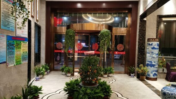 Un hall d’hôtel agrémenté d’un grand arrangement floral central, d’un comptoir d’accueil et d’une grande porte vitrée avec une signalétique.