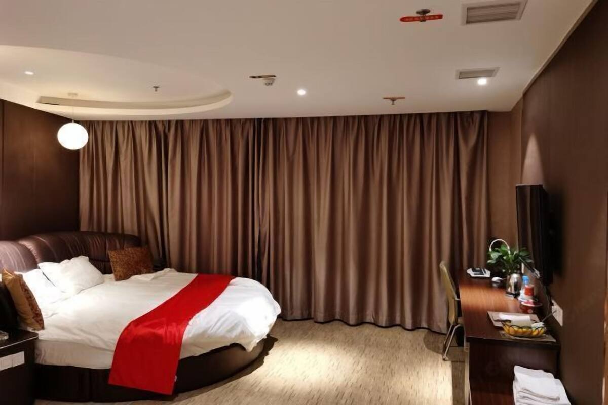 A hotel room with a large bed, a desk, a chair, a TV, and a curtain.